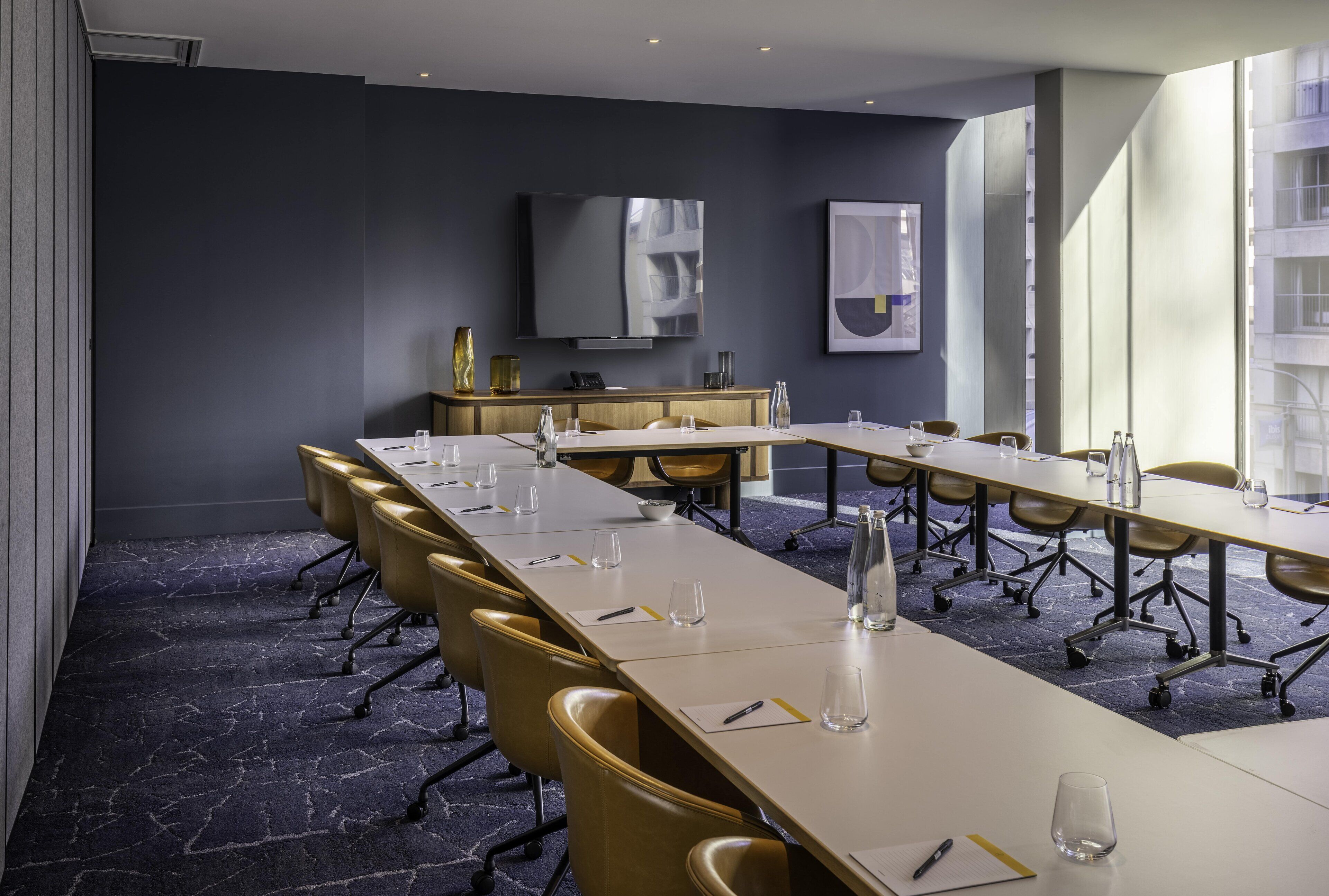 A conference room with a long table, chairs, a flat-screen TV, and a large window.