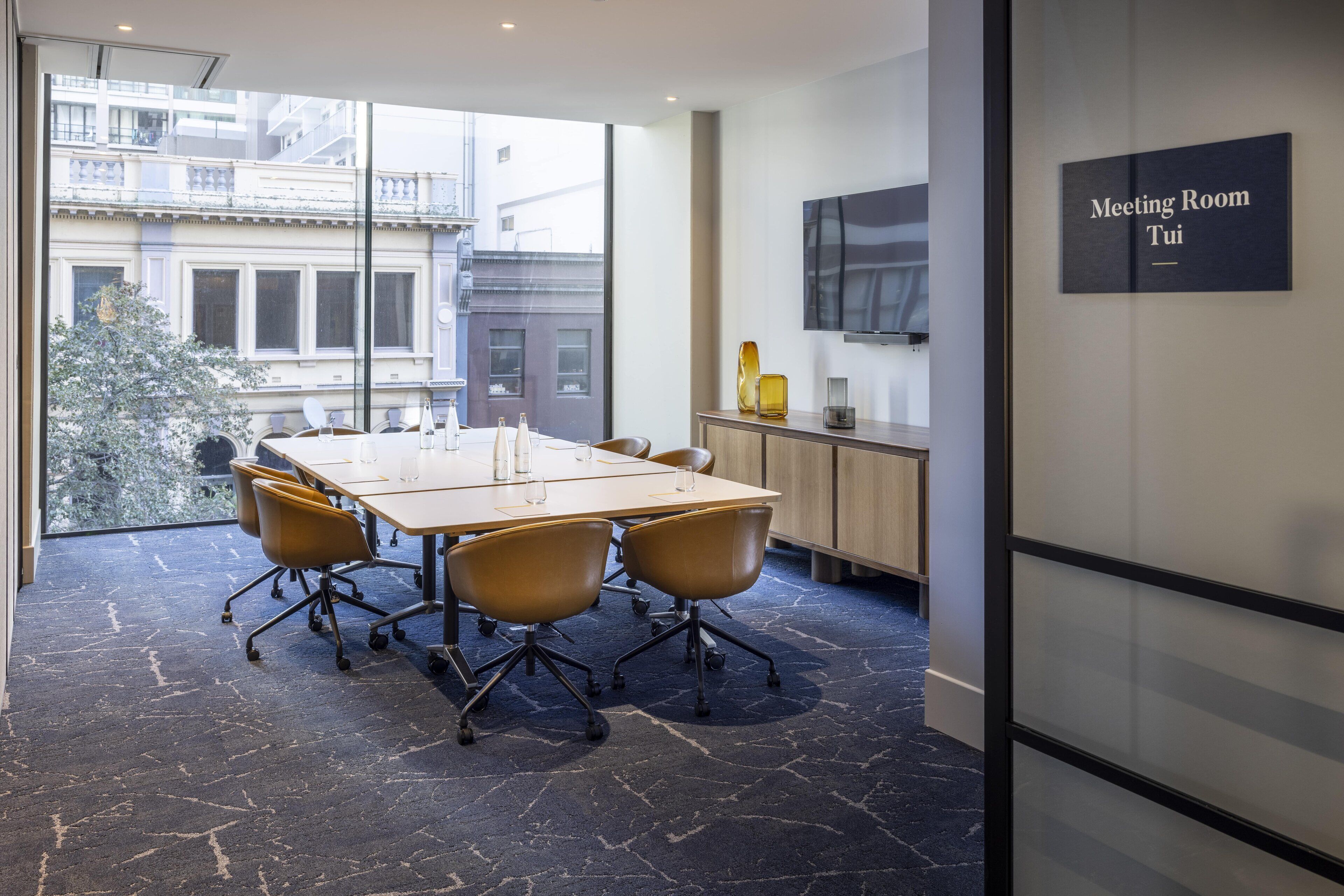 A meeting room with a large table, four chairs, a TV, and a sign indicating it's the meeting room.