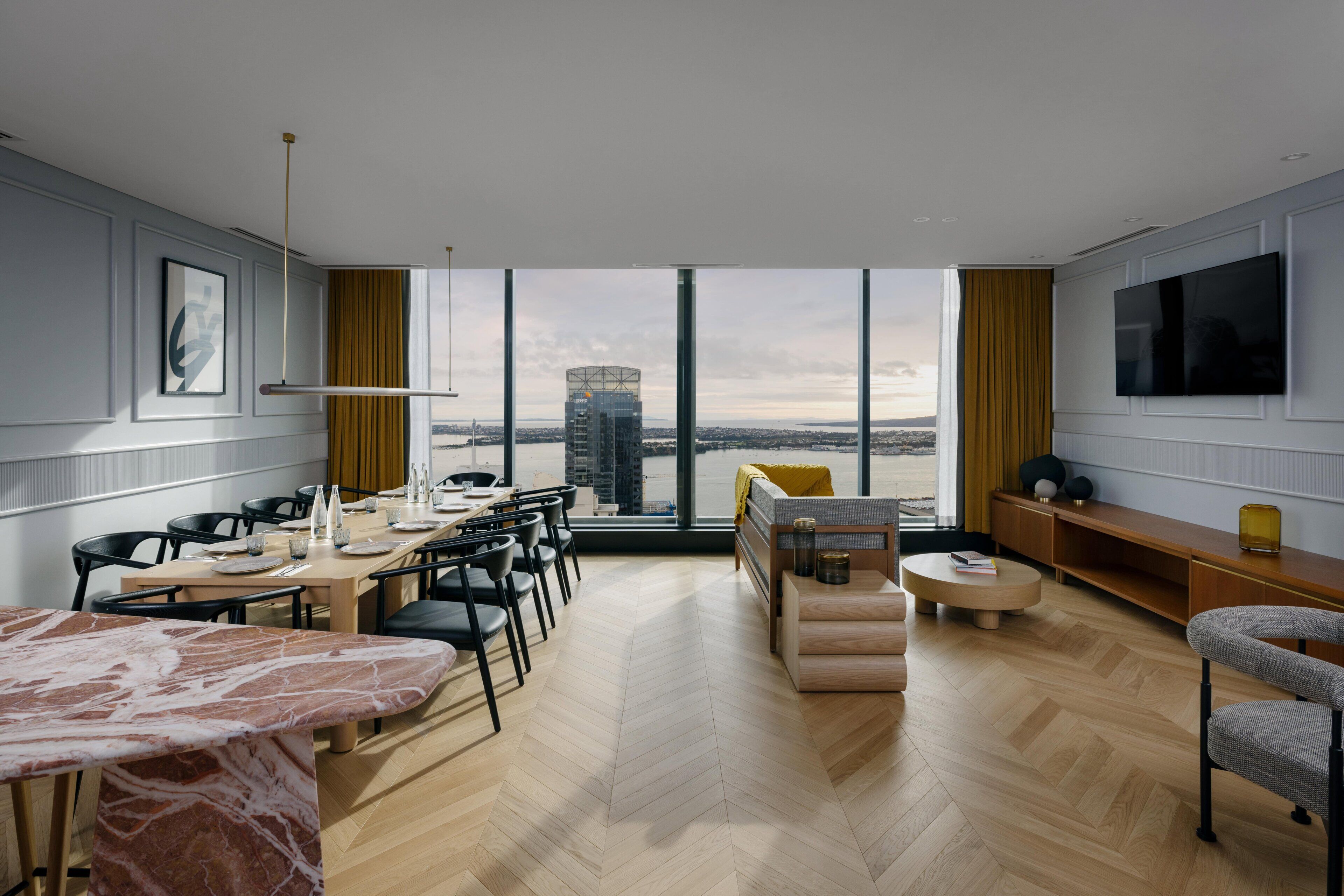 Een moderne woonkamer met een eethoek, grote ramen met uitzicht op de stad, een flatscreen aan de muur en een bank met uitzicht.