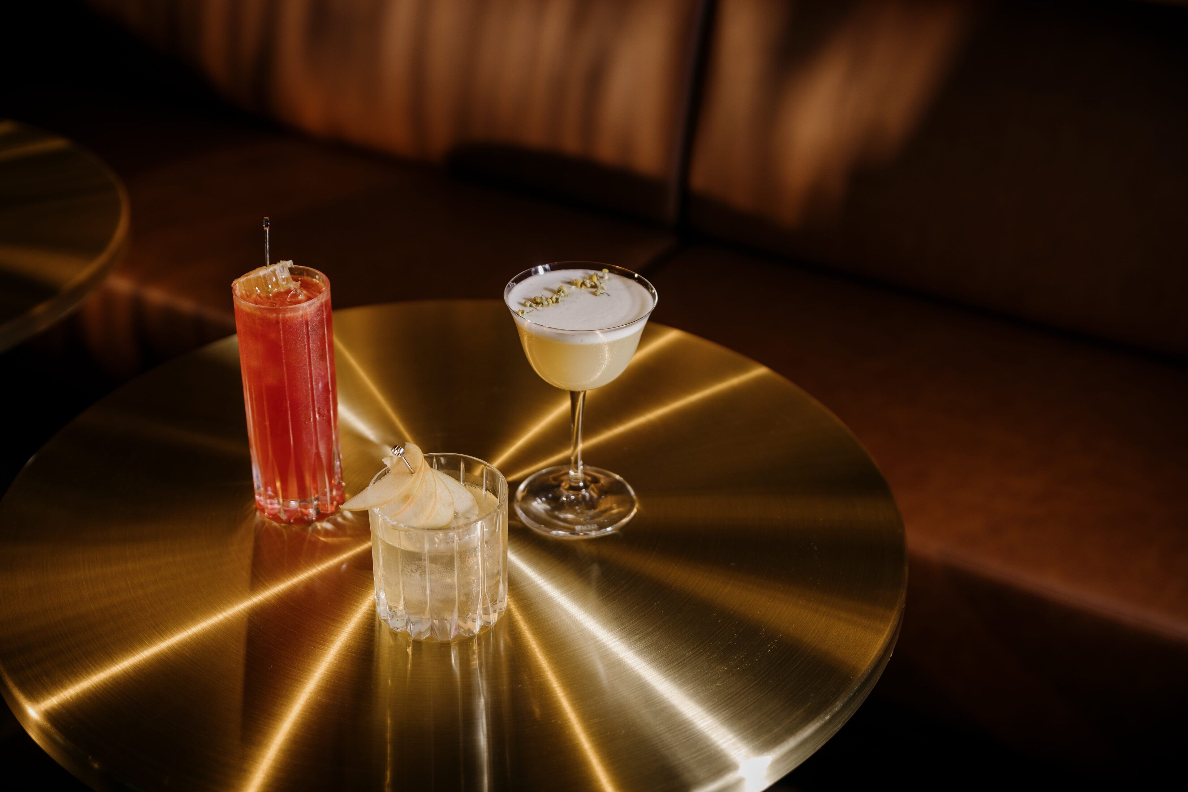 Three drinks on a metallic table with a sofa in the background.