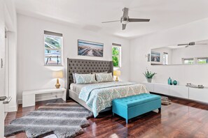 Une chambre avec un grand lit, un ventilateur de plafond, un banc et un tapis.