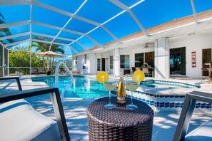 Un espace piscine abrité avec des chaises longues, une table avec des boissons et une vue sur la piscine.