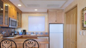 A kitchen with wooden cabinets, a microwave, a refrigerator, and a sink. There are two chairs at the counter. - Located on the pristine Medano beach (Cabo San Lucas)