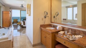 A hotel bathroom with a large mirror, a bathtub, a sink, and a vanity. There is a balcony with a view of the ocean. - Located on the pristine Medano beach (Cabo San Lucas)