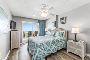 A bedroom with a bed, nightstands, a ceiling fan, and a view of the outdoors. - Ocean House 1304 | Heated, Zero Entry Pool | Oceanfront Balcony | My Beach Getaways (Gulf Shores)