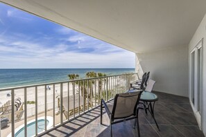 A balcony with a view of the beach, a pool, and a table with chairs. - Ocean House 1304 | Heated, Zero Entry Pool | Oceanfront Balcony | My Beach Getaways (Gulf Shores)