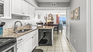A compact kitchen with white cabinets, a dishwasher, and a stove. - Ocean House 1304 | Heated, Zero Entry Pool | Oceanfront Balcony | My Beach Getaways (Gulf Shores)