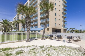 A multi-story hotel with balconies, palm trees, and outdoor barbecue grills. - Ocean House 1304 | Heated, Zero Entry Pool | Oceanfront Balcony | My Beach Getaways (Gulf Shores)