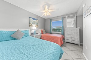 A bedroom with two beds, a ceiling fan, a window with blinds, a dresser, and a wall-mounted mirror. - Ocean House 1304 | Heated, Zero Entry Pool | Oceanfront Balcony | My Beach Getaways (Gulf Shores)
