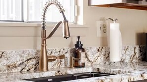 Una cocina con encimera de mármol, grifo moderno y armarios de madera.
