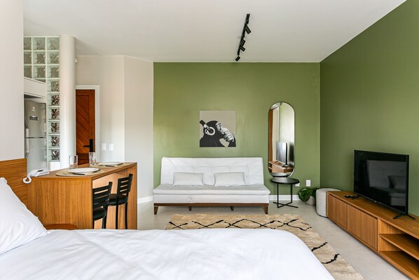 Una habitación de hotel moderna con una cama, un escritorio con sillas, un sofá, un televisor y un espejo.