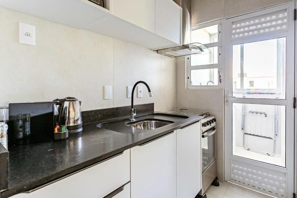 A compact kitchen with a black countertop, stainless steel sink, and a built-in oven.