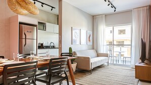 Un salon moderne comprenant un coin repas, un canapé, un téléviseur et une grande fenêtre avec des rideaux.
