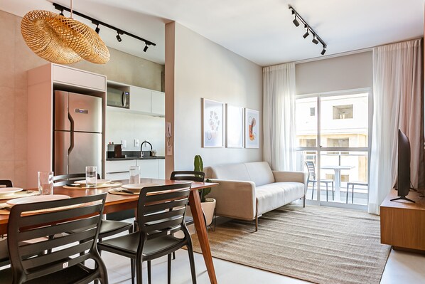 A modern living room with a dining area, a sofa, a TV, and a large window with curtains.
