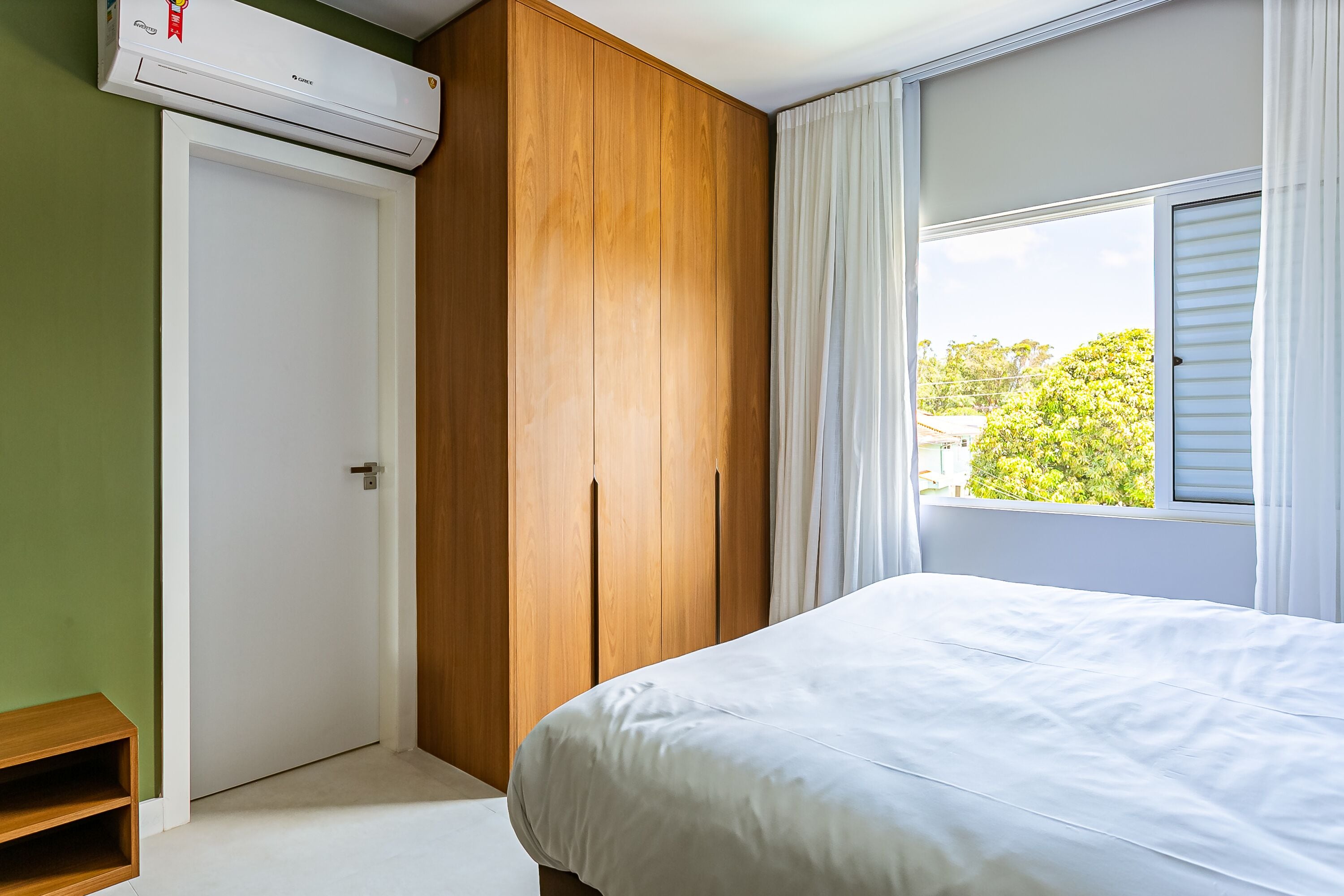 Un dormitorio con cama, armario, ventana con cortinas y equipo de aire acondicionado.