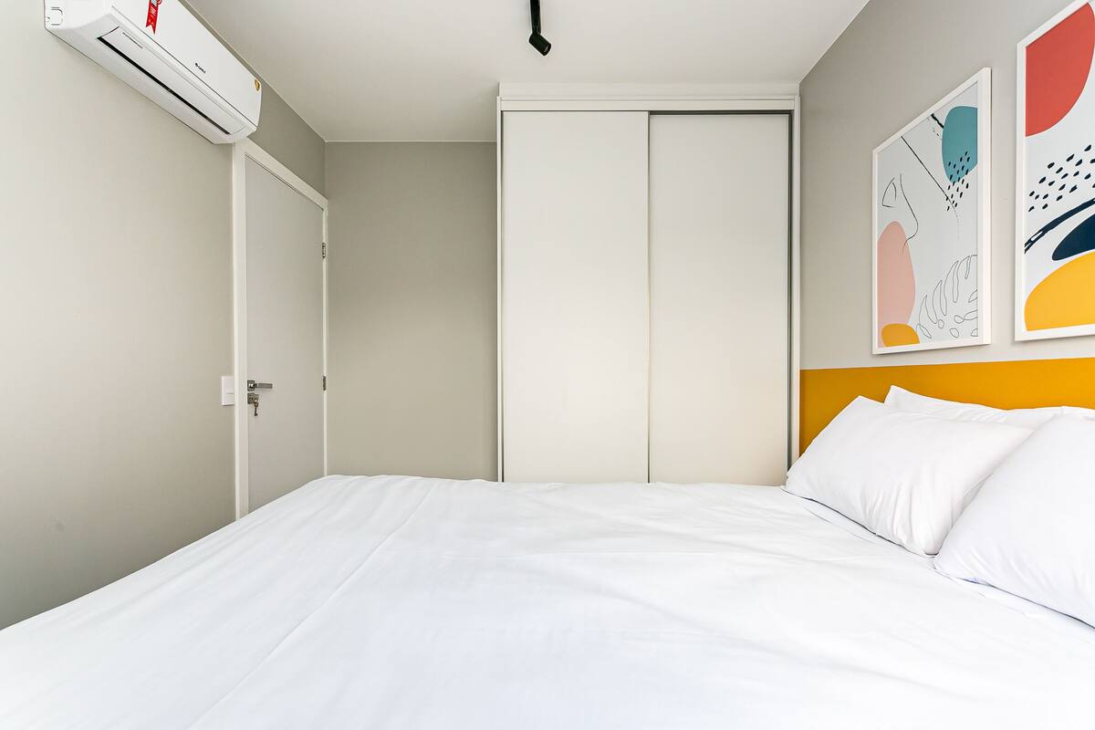 Un dormitorio con cama, aire acondicionado, una puerta y arte abstracto en la pared.