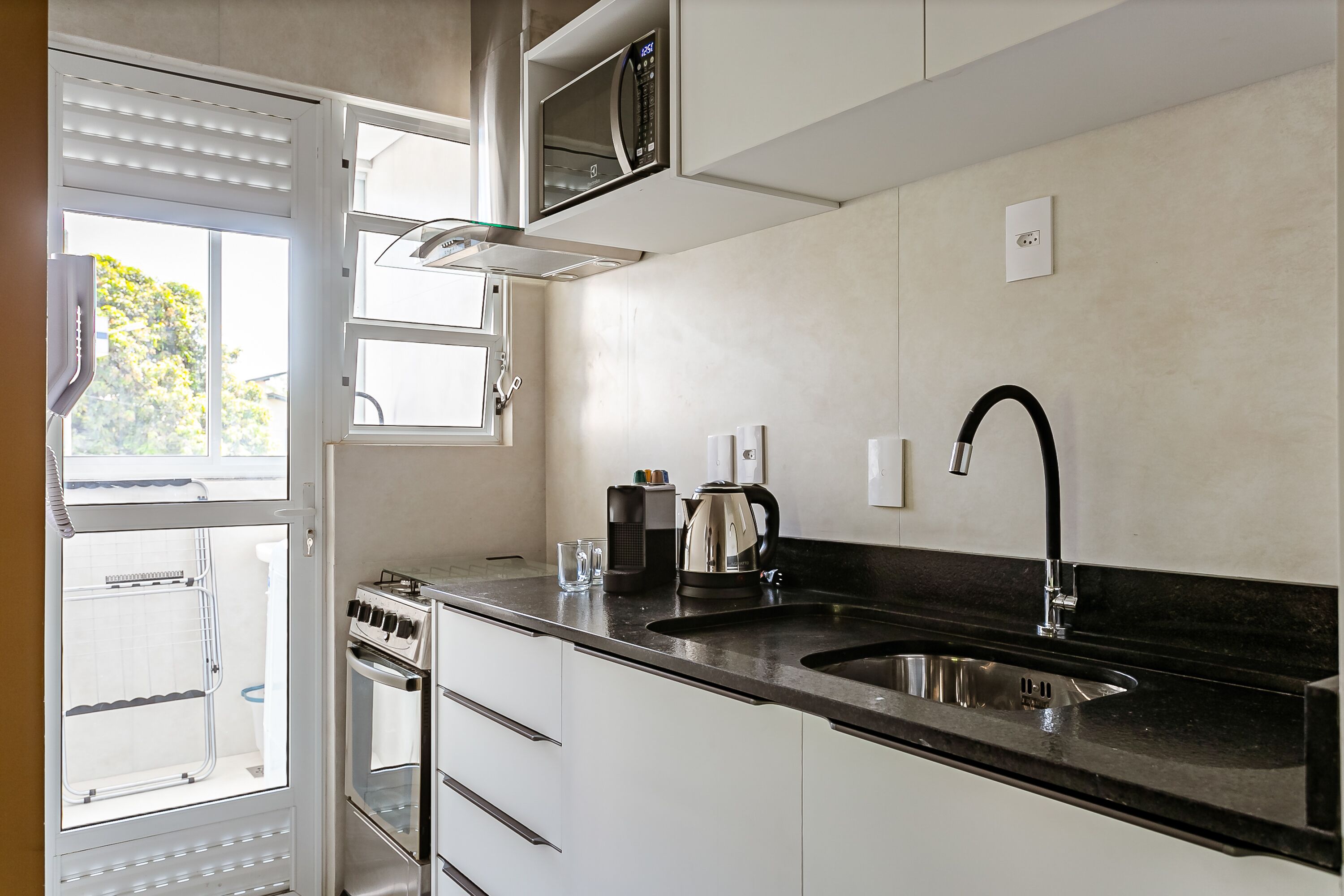 A modern kitchen with a black countertop, stainless steel sink, and built-in oven.