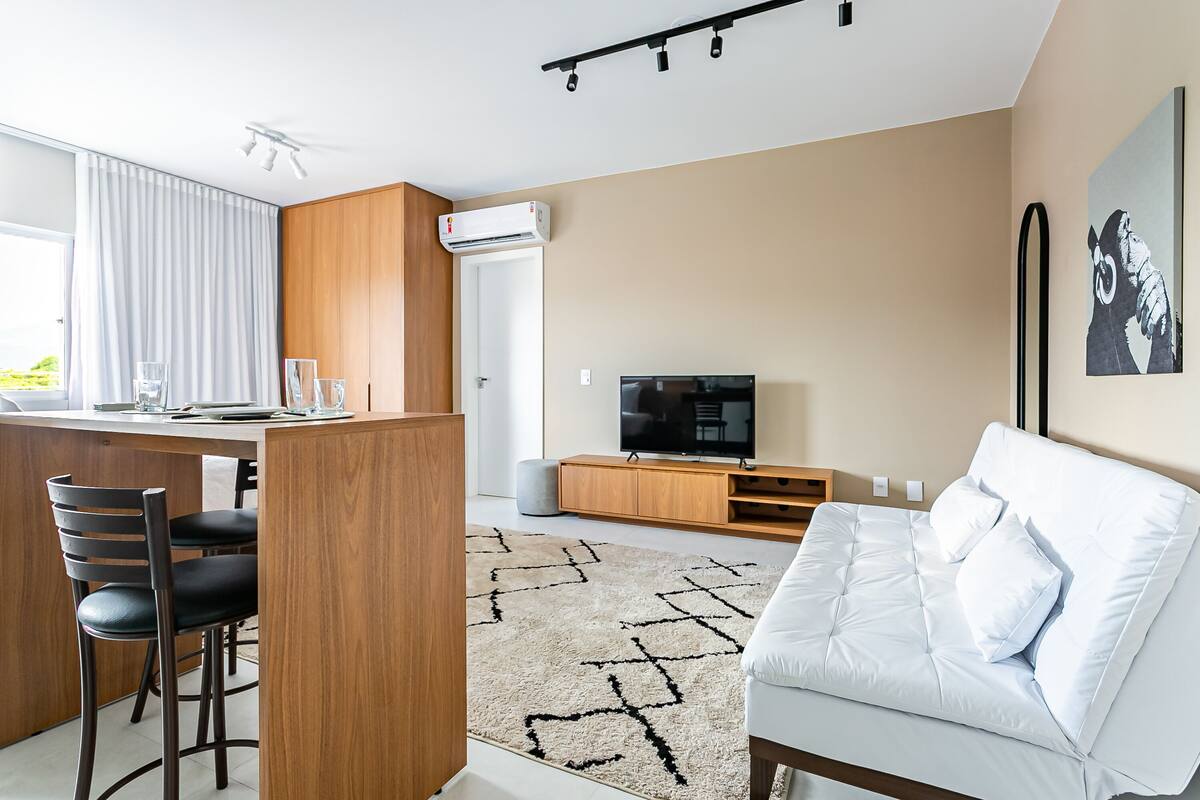 Un espacio habitable moderno con una zona de cocina, un sofá blanco y un televisor.