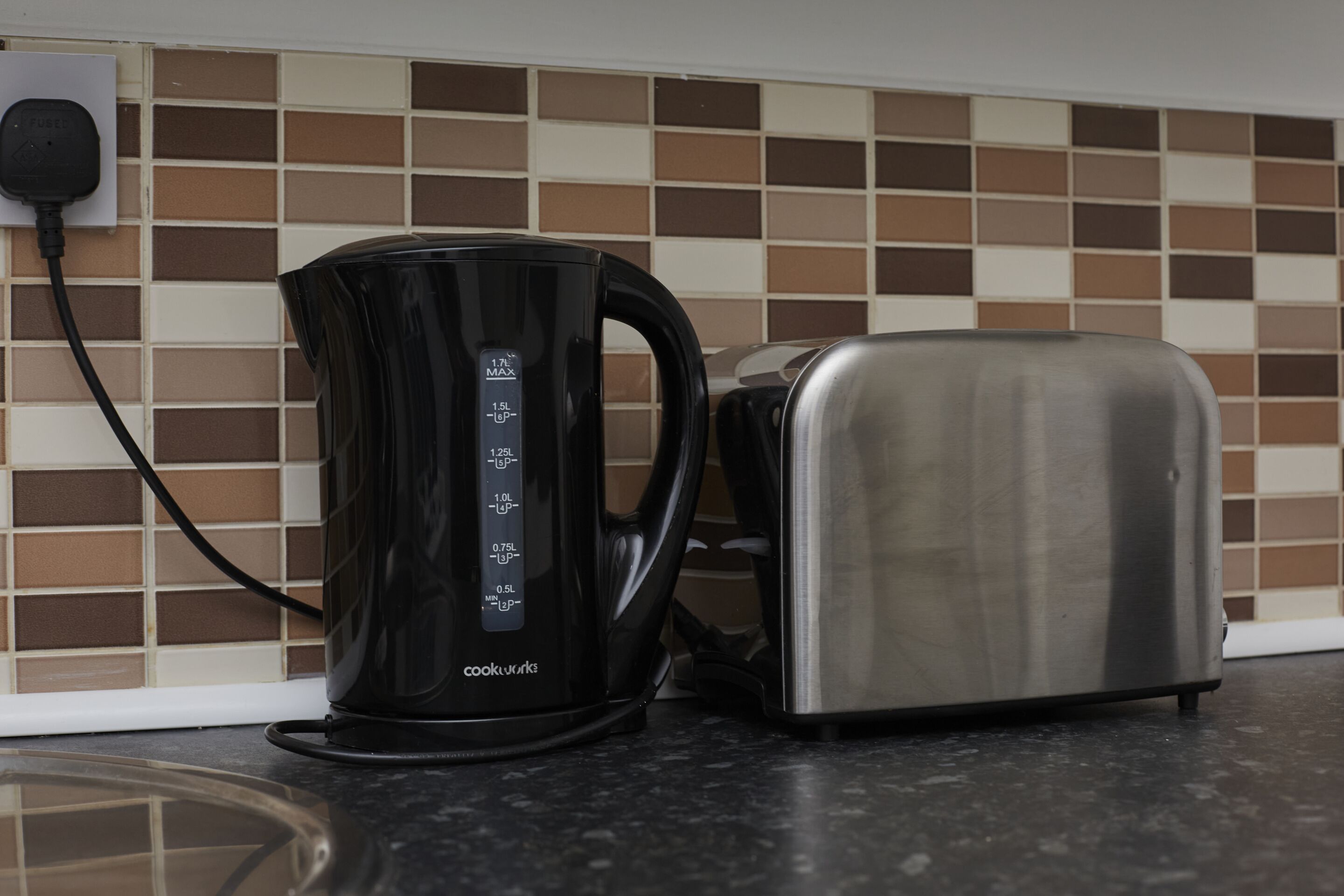 Eine Küche mit einem schwarzen Wasserkocher und einem Edelstahltoaster auf einer schwarzen Arbeitsfläche.