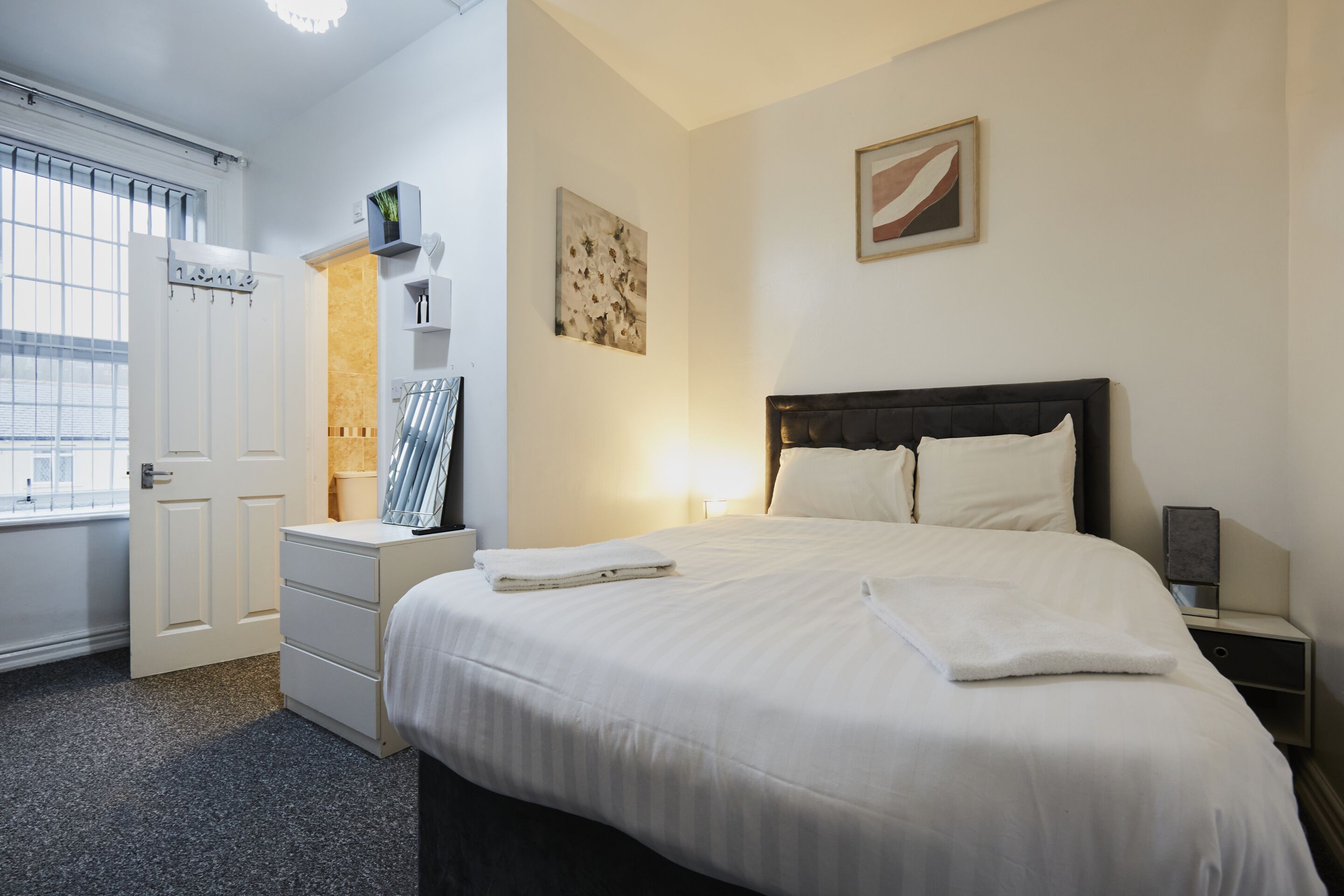 Una habitación de hotel con una cama, una mesita de noche, un aparador, una ventana con persianas y un cuadro en la pared.