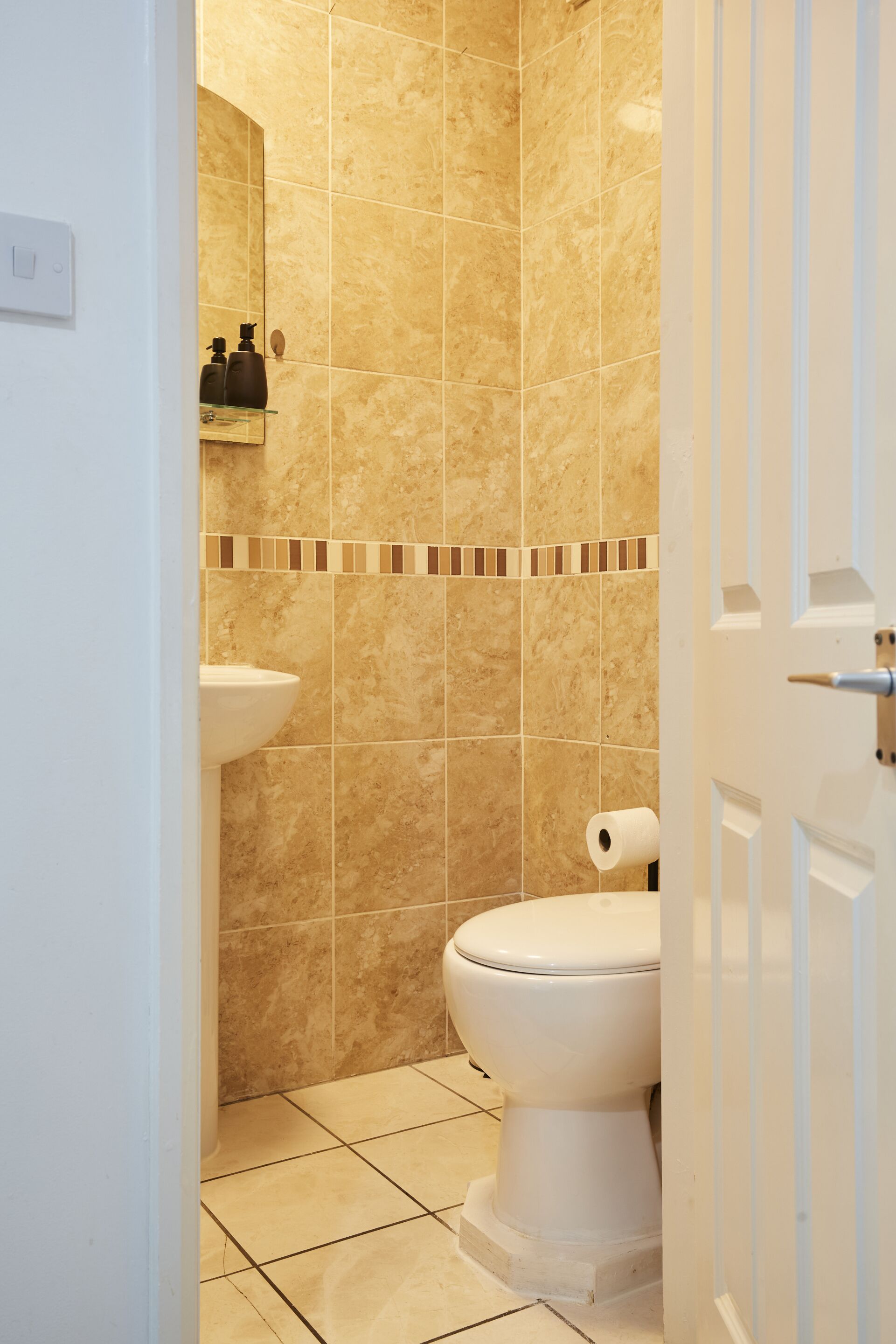 A bathroom with beige tiles, a white toilet, and a mirror above the sink.
