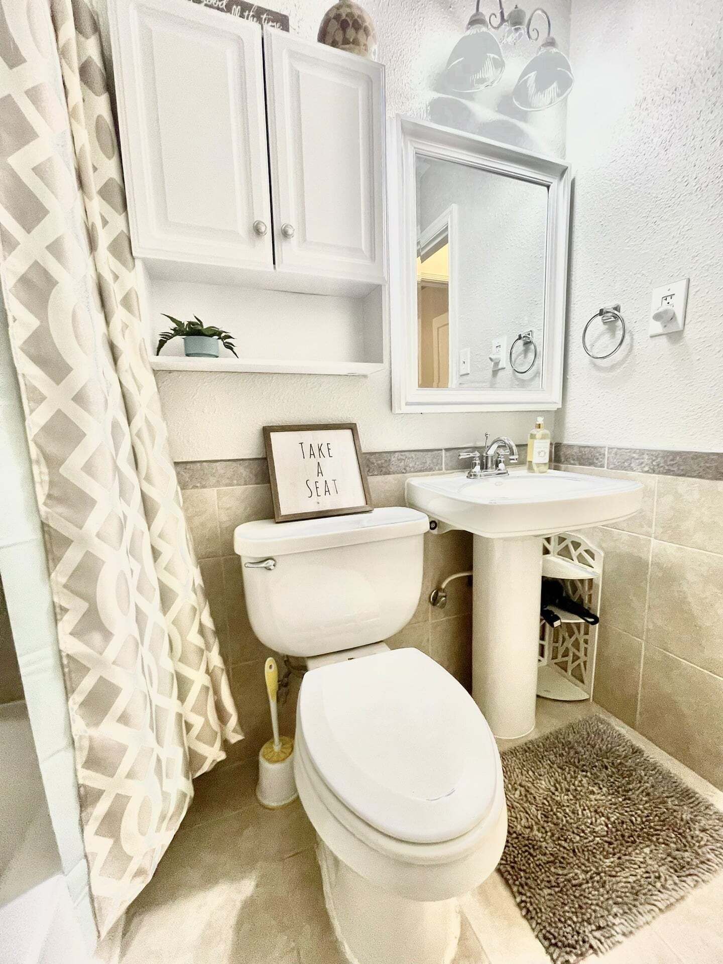 Une salle de bain avec des toilettes, un lavabo et un miroir. Il y a une pancarte sur les toilettes qui indique : « Asseyez-vous. »