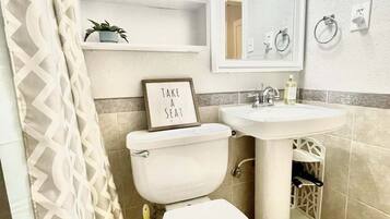 Une salle de bain avec des toilettes, un lavabo et un miroir. Il y a une pancarte sur les toilettes qui indique : « Asseyez-vous. »