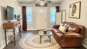 A living room with a brown leather sofa, a glass coffee table, a wooden side table, a television, and a ceiling fan. - 3-bedroom vacation home 12 minutes from Paycom Center (Midwest City)