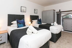 A hotel room with two beds, grey headboards, white bedding, and a grey wardrobe.
