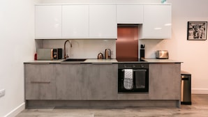 A modern kitchen with white cabinets, a stainless steel range hood, a built-in oven, and a microwave. - Strawberry Line, Flat 1 (Wells)