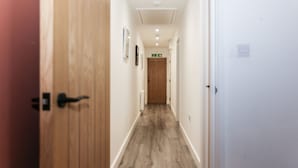 A hallway with wooden flooring, white walls, and a door at the end. - Strawberry Line, Flat 1 (Wells)