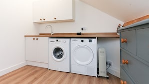 A compact laundry area with a washing machine and dryer, wooden flooring, and a white cabinet above. - Strawberry Line, Flat 1 (Wells)