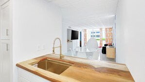 A modern kitchen with a wooden countertop, a gold faucet, and a view into a dining area with a white table and chairs. - Retro Condo Extreme High End finishings (Scottsdale)