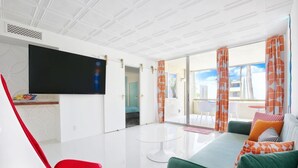 A modern living room with a flat-screen TV, a red chair, a green sofa, and a balcony with orange curtains. - Retro Condo Extreme High End finishings (Scottsdale)