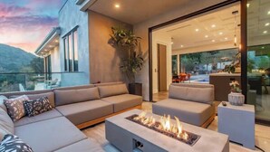 A modern outdoor living area with a fire feature, sofas, and a glass door leading to an interior space.