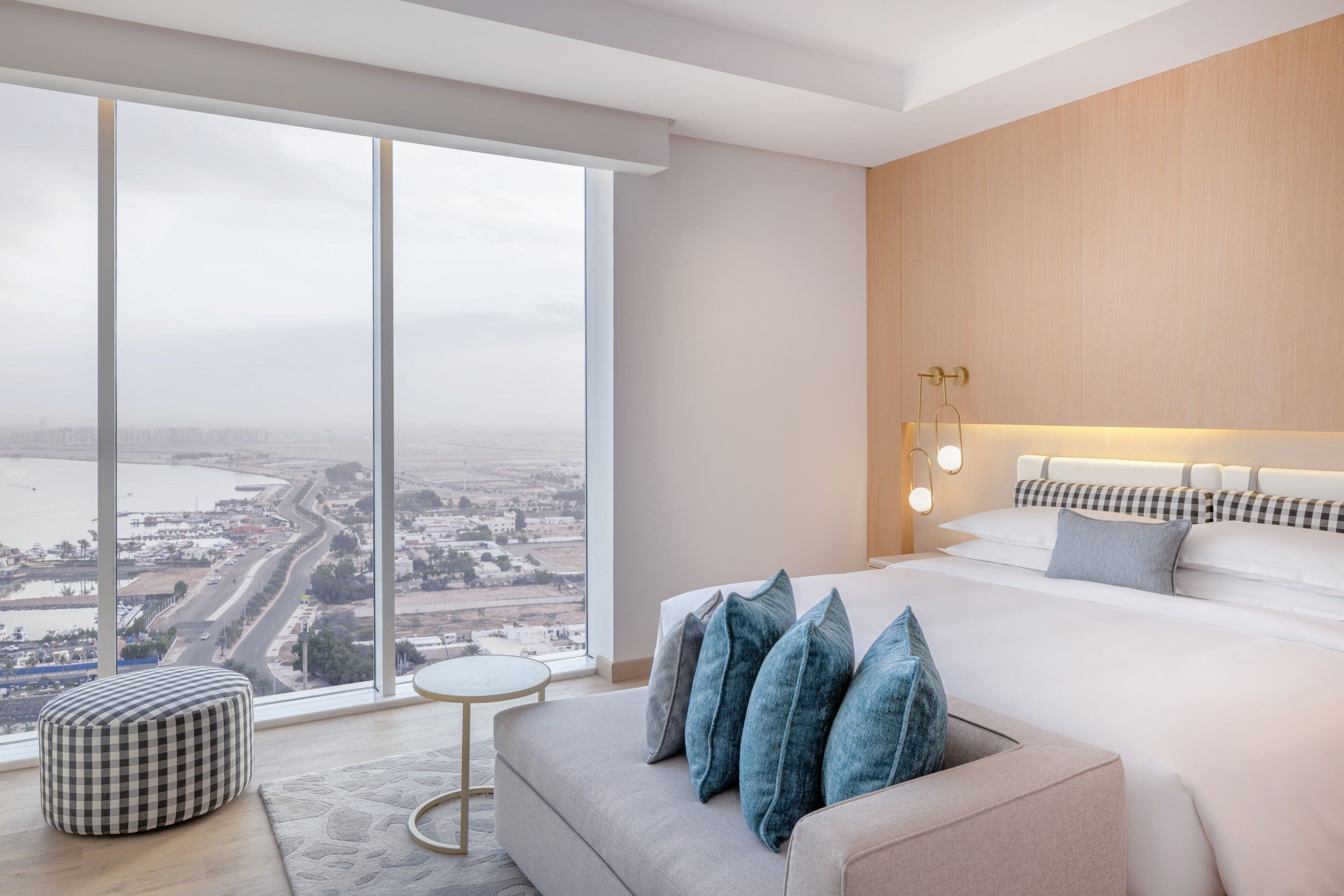 Een moderne hotelkamer met een groot raam, een bed, een slaapbank en een klein, rond tafeltje.