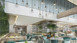 Un restaurante moderno con techos altos, lámparas colgantes y una variedad de zonas de estar, incluyendo reservados y mesas.
