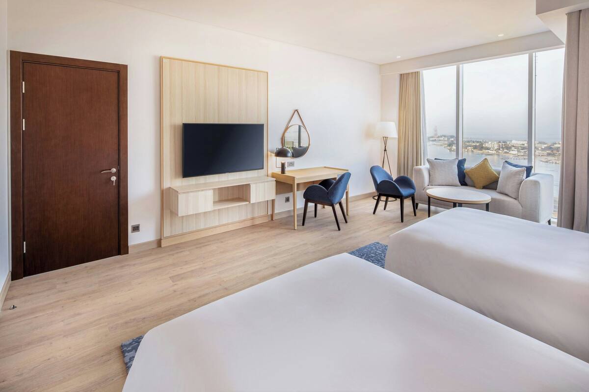 A hotel room with a large bed, a desk with a chair, a TV, and a view of the city.