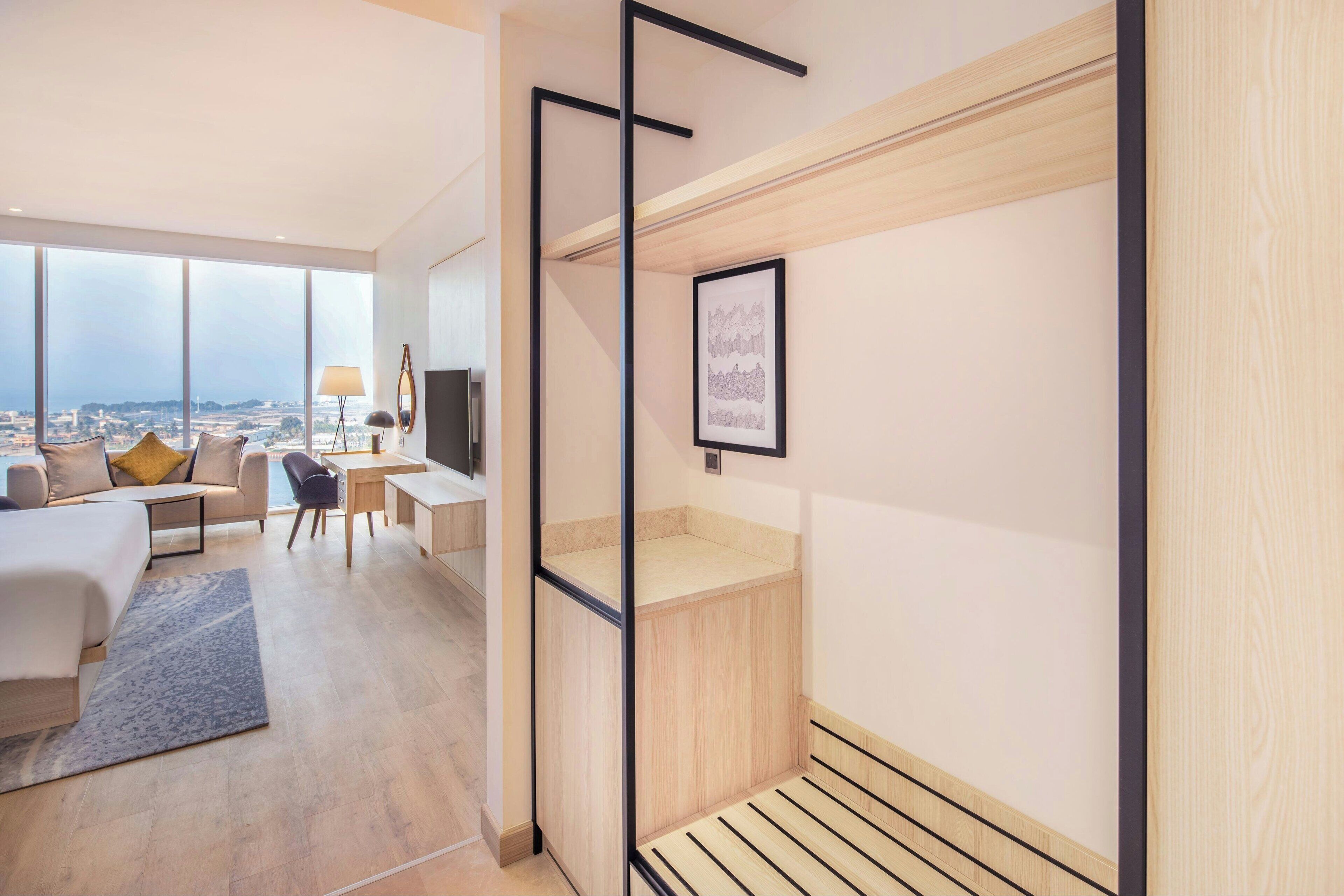 A modern hotel room with a large window, a bed, a desk, and a chair.