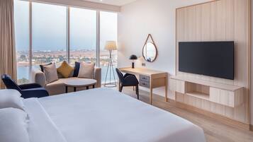 A hotel room with a large bed, a desk, a chair, a TV, and a view of the city.