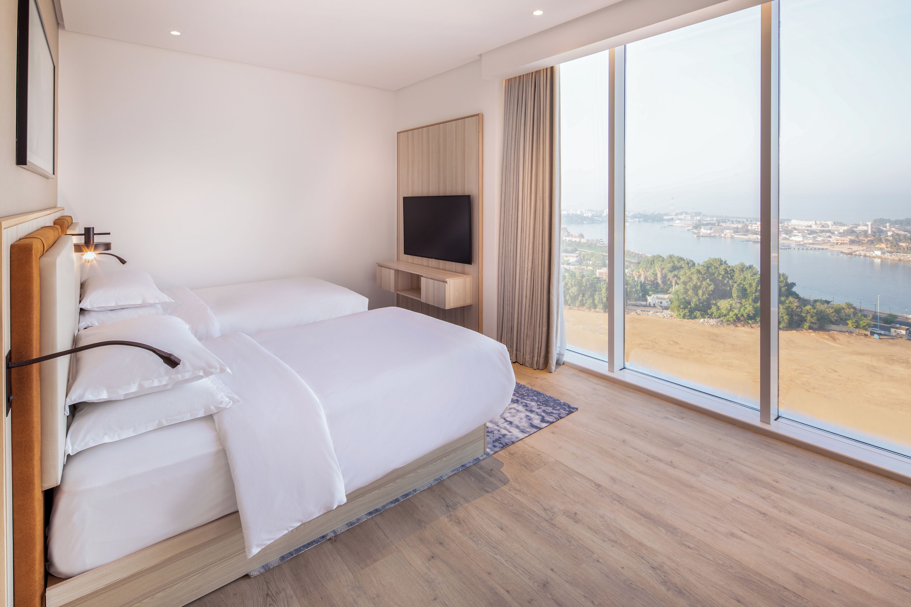 A modern hotel room with a large bed, a flat-screen TV, and a scenic view of a body of water.
