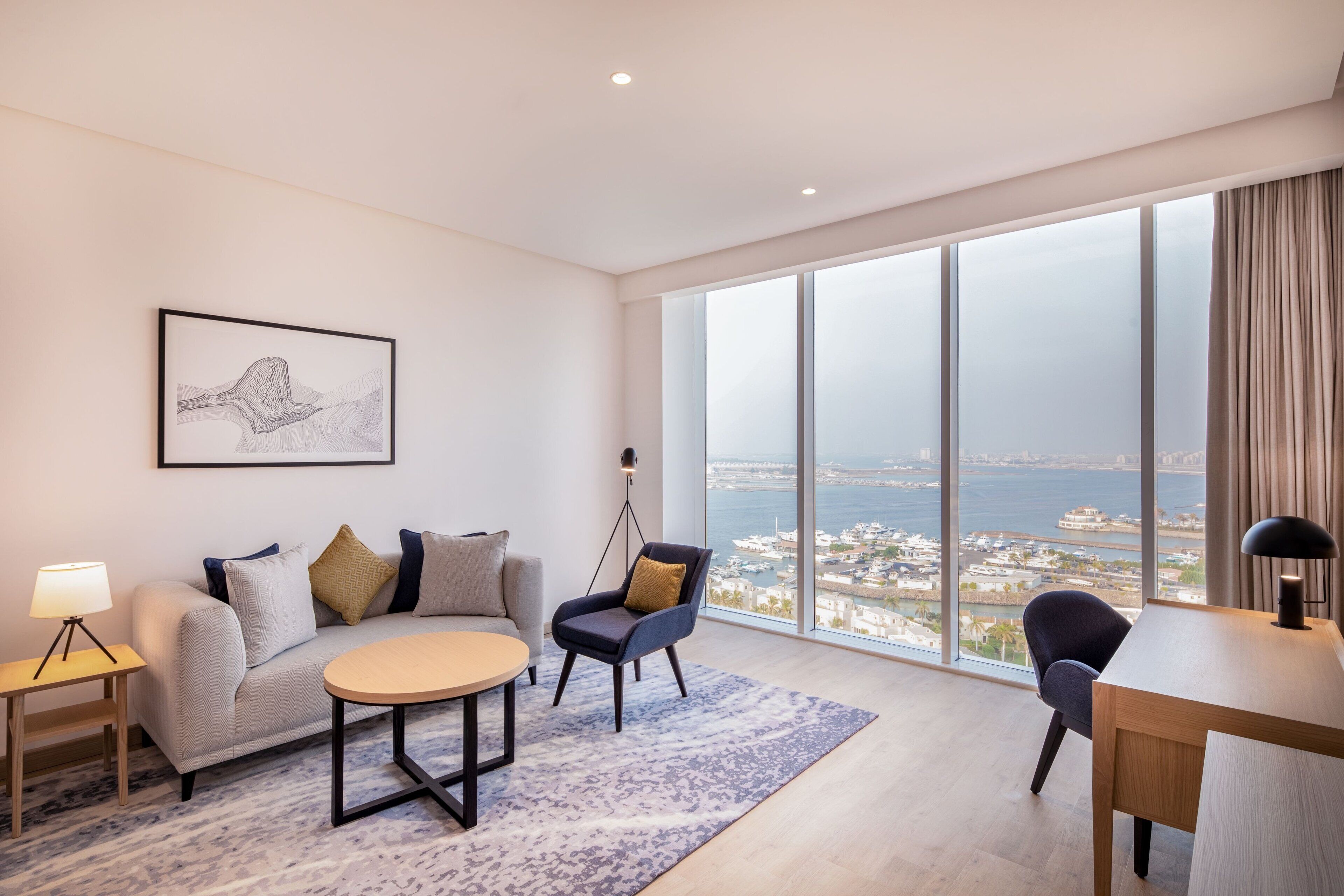 Una sala de estar moderna con sofá, sillón y mesa de centro, un escritorio y un ventanal con vistas a la ciudad.