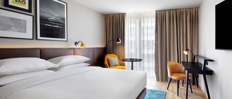 A hotel room with a large bed, a desk with two chairs, a small table, and a TV mounted on the wall.