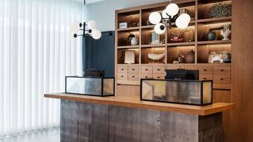 A modern reception desk with two black radios, a wooden display cabinet with decorative items, and a large window with sheer curtains.
