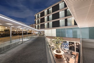 A modern hotel atrium with a covered outdoor seating area, a central staircase, and a view of the building's exterior.