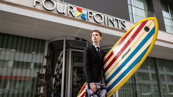 A man holding a surfboard in front of a building with the sign "FOUR POINTS BY SHERATON".