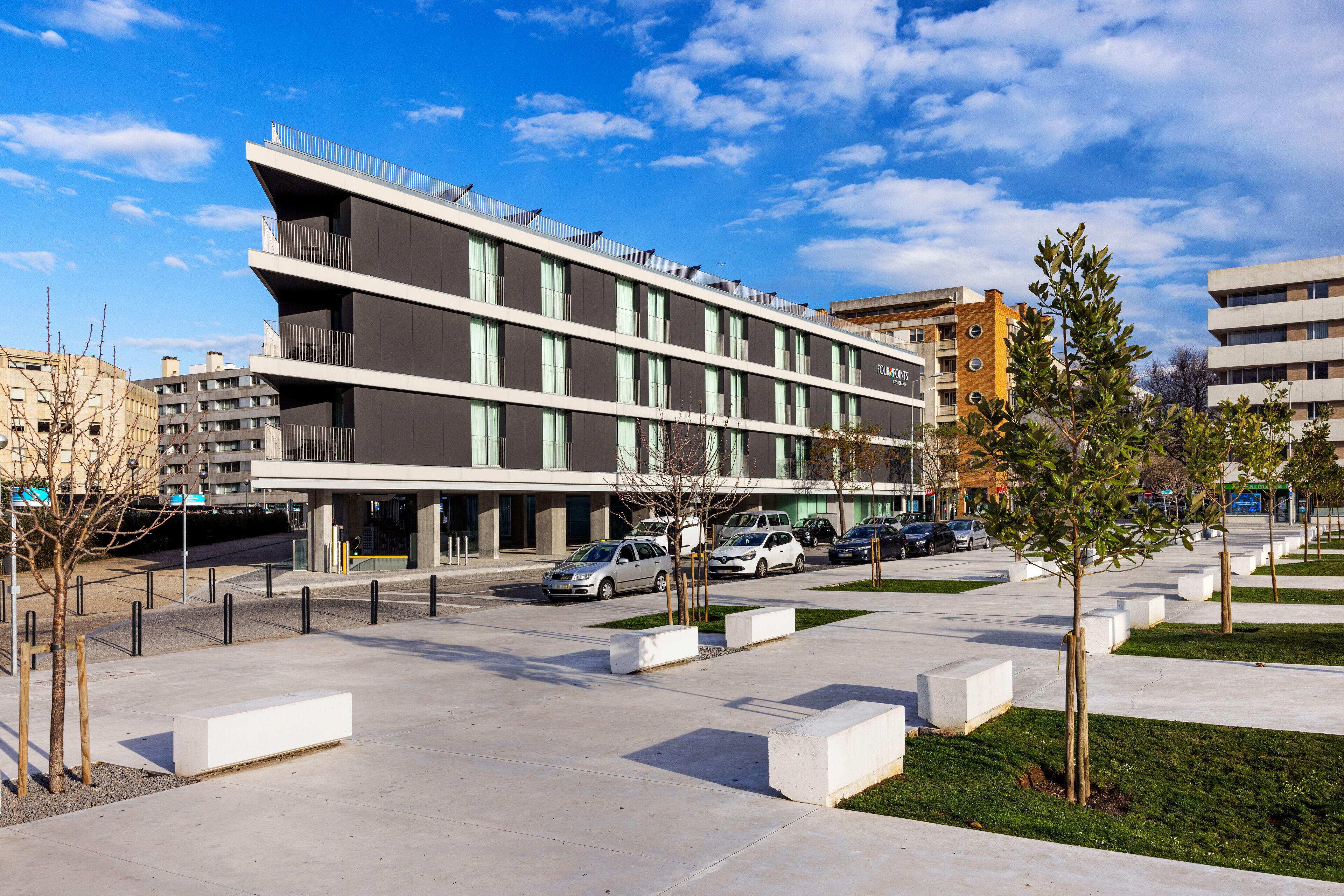 Un edificio moderno de varios pisos, con amplias ventanas y un estacionamiento con coches.