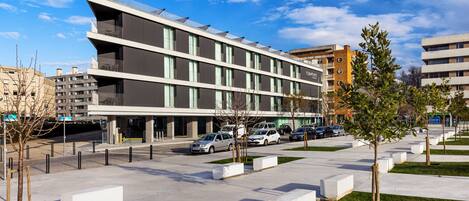 Un edificio moderno de varios pisos, con amplias ventanas y un estacionamiento con coches.