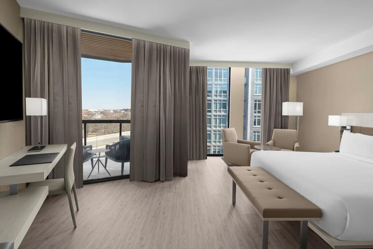 Ein Hotelzimmer mit einem großen Bett, einem Schreibtisch, einem Stuhl und Blick auf die Stadt.