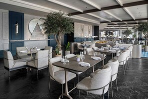 A modern dining area with round tables, cushioned chairs, and a large potted tree. - AC Hotel by Marriott Washington DC Capitol Hill Navy Yard (Washington)